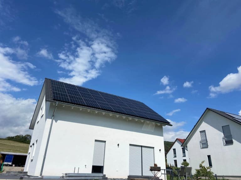Neubau-Einfamilienhaus mit weißer Fassade und schwarzen Solarmodulen auf dem Satteldach
