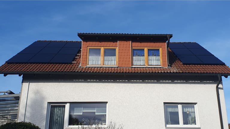 Satteldach eines Wohnhauses in Erbsen mit Gaube, links und rechts davon schwarze Solarmodule unter blauem Himmel