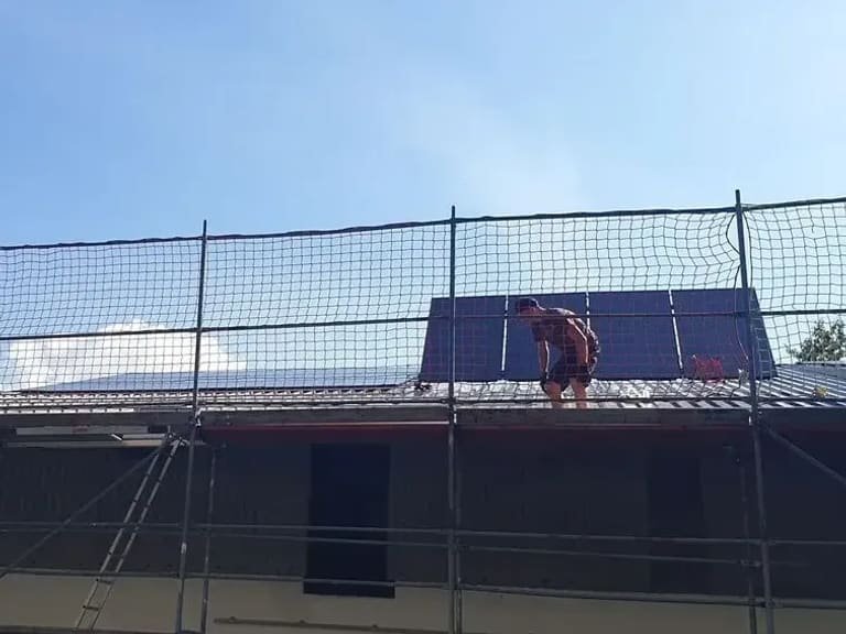 Montage im Gange: ein Monteur kniet auf dem Dach neben dem bereits verlegten Modulfeld, davor das Gerüst