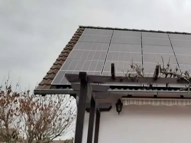 Ziegeldach über die volle Breite mit Solarmodulen belegt, darunter die Balken einer Pergola